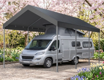 Silver RV parked under a large gray carport with cherry blossoms in the background