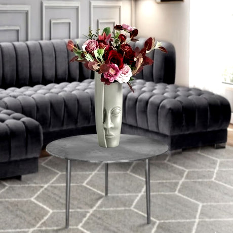 Gray tufted sofa with a round metal table and floral arrangement in a room with hexagonal gray tiles.