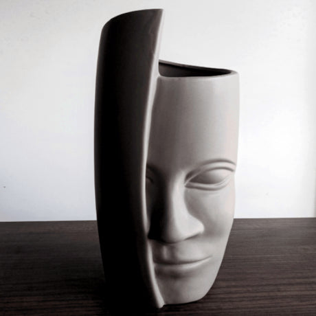 Ceramic vase shaped like a face on a wooden surface with a white background