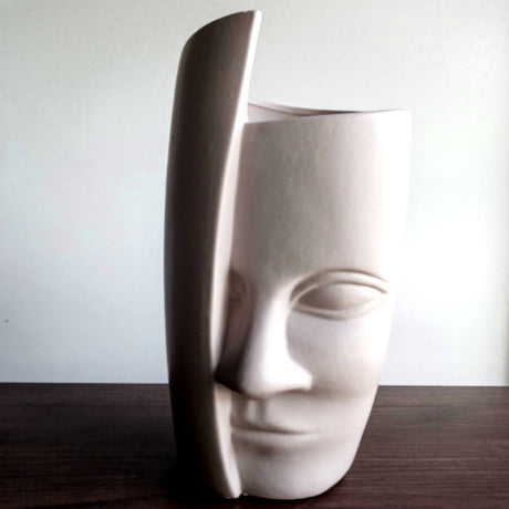 White ceramic vase shaped like a face on a wooden surface with a white background
